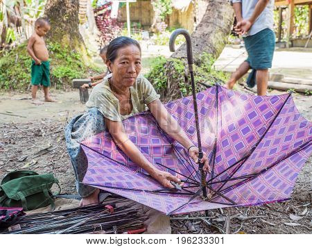 Rakhine State Myanmar - October 14 2014: Umbrella repair woman in a village along the Lemro River in the Rakhine State of Myanmar. Most places in Myanmar getting a broken umbrella repaired is not a problem.