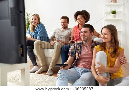 friendship, leisure, people and entertainment concept - happy friends with remote control and drinks watching tv at home