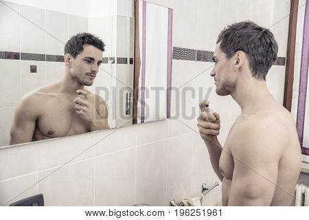 Handsome young man in his home bathroom, spraying cologne or perfume on neck