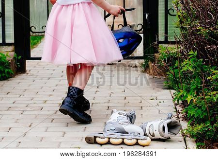 Active outdoor sport for kids. Young girl is holding a helmet for roller skating in a pink fluffy skirt, at the feet lie roller skates.Inline skates sport conceptual image.