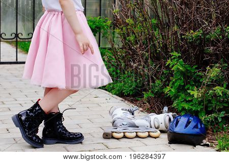Active outdoor sport for kids. Young girl is holding a helmet for roller skating in a pink fluffy skirt, at the feet lie roller skates.Inline skates sport conceptual image.