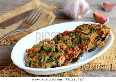 Crispy fried eggplant cutlets with garlic and dill on a white plate and a burlap textile. Fork and knife on a vintage wooden background. Gluten-free fried eggplant cutlets recipe. Closeup