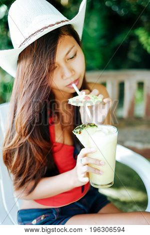 Beautiful girl with the hat dringking fresh and refreshing pineapple juice summer holiday vacation