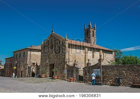Monteriggioni, Italy - May 13, 2013. People and church at the hamlet of Monteriggioni. A medieval fortress, surrounded by stone walls, at the top of a hill, near Siena. Located in the Tuscany region