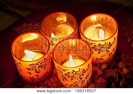 Four lit candles in decorated glasses on plate viewed from above