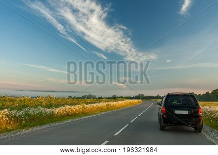 Black Car On Asphalt Road Under Blue Sky In Early Summer Dense Fog Sunny Dawn.