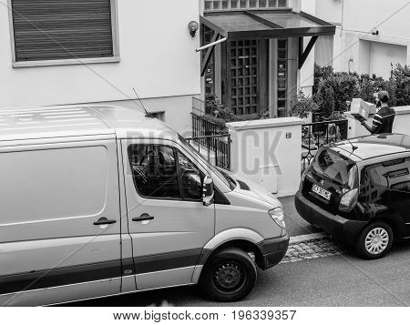 PARIS FRANCE - JUL 12 2017: Black and white Aerial view of delivery man with cardboard parcel box writing info notice to absent client to come back later to the the consignee to deliver the cardboard parcel