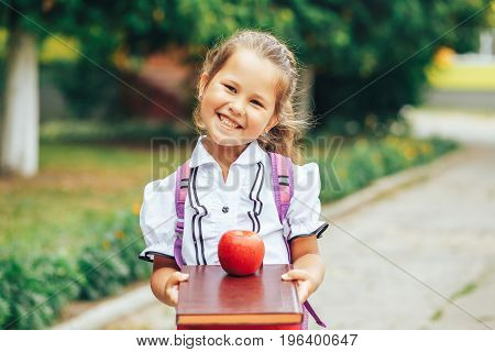 A cute girl is holding a book with a red apple