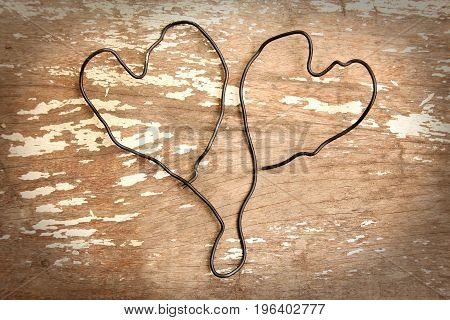 Wire bent in shape of two heart togather on wooden background.