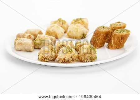 Crispy assorted baklava bites arranged on a plain plate. Five pieces of Kol W Shkor cashew baklava decorated with chopped pistachio crumbs in the front. Closeup studio shot on white background.