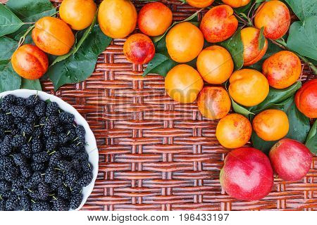 On the wicker table lie orange apricots and a plate with mulberry.