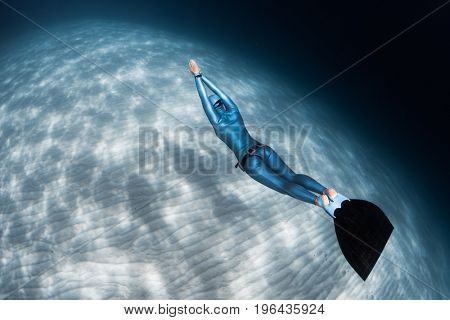 Woman freediver glides over sandy sea bottom with monofin