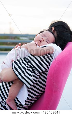Mother holding her newborn baby in sexy dress while her was sleeping. Baby is sleeping on her mother shoulder at the rooftop. Mother day bonding concept with newborn baby nursing.