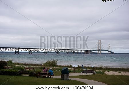 MACKINAW CITY, MICHIGAN / UNITED STATES - JUNE 18, 2017:  Visitors may sit in Alexander Henry Park, and enjoy the view of the Mackinac Bridge, which spans the Straits of Mackinac, to connect Michigan's Lower and Upper Peninsulas.