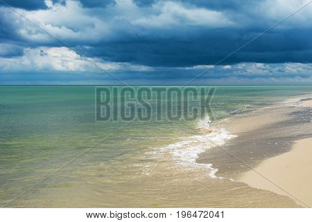 Seaside with small waves and dark clouds over water.