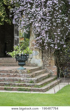 Beautiful English Country Garen Landscape Image Wth Hanging Flowers And Vintage Steps And Plant Urns