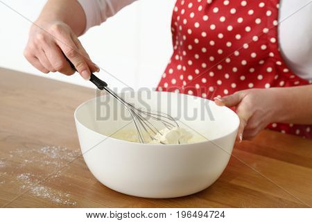 Woman's hand holding whisk mixing cream cheese in plastic bowl