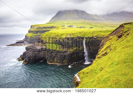 Dramatic waterfall in rainy weather on Faroe Islands and the village Gasadalur in the background.