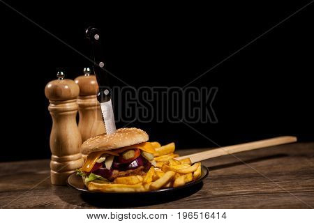 Classic home made cheesburgers on black plate and background next to fries. Fast food. Unhealthy snack