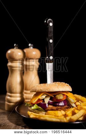 Classic home made cheesburgers on black plate and background next to fries. Fast food. Unhealthy snack