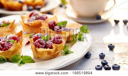 Phyllo cups with Mascarpone filling topped with raspberries on a white plate