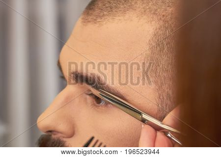 Scissors cutting eyebrow of man. Brow grooming close up.