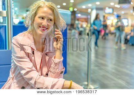 Businesswoman at boarding gate, sitting talking on smartphone. Woman using mobile phone app for conversation. Female enjoing in airport while waiting to get on air flight.Blurred background.Copy space
