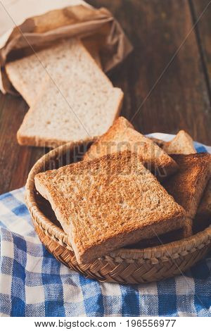 Breakfast background, white bread toasts in wicker breadbasket on checkered table napkin half covering wooden table, closeup, vertical