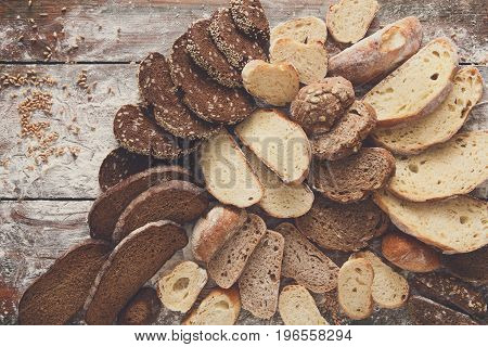 Sliced bread background on rustic wood, copy space. Brown and white loaves and flour top view composition with wheat flour sprinkled around.