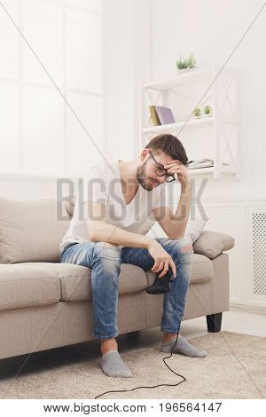 Sda young man playing video games at home and loses. Guy sitting on the couch with joystick in hands, copy space