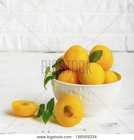 Yellow plums in a white ceramic bowl against a white kitchen brick wall. Selective focus