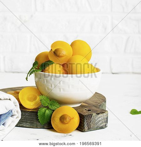 Yellow plums in a white ceramic bowl against a white kitchen brick wall. Selective focus
