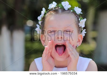 little girl showing tongue and covers his face with his hands a child with a wreath of artificial flowers on her head