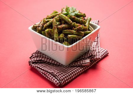 A Masala or fried vegetable dish consisting of green beans, onions, and curry spices, served in square bowl, selective focus