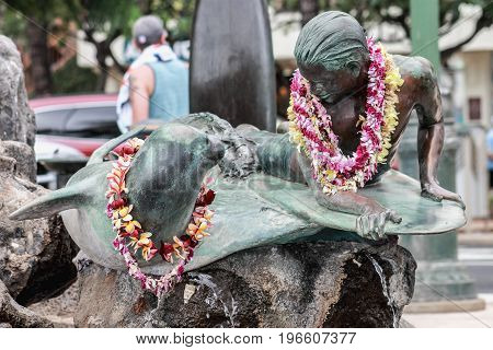 Honolulu Hawaii USA - May 28 2016: Makua and Kila bronze statue - public art sculpture shows a young surfer (Makua) sharing a moment with a monk seal (Kila).