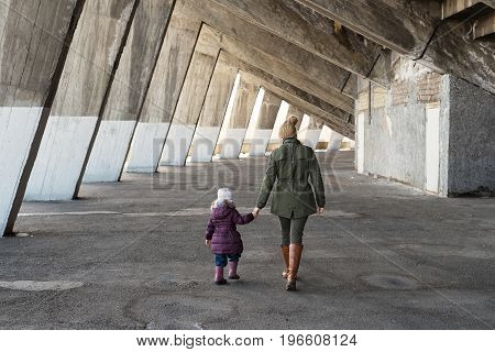 Mother and daughter walking hand in hand in an old massive grunge constraction.