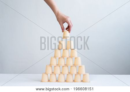Female hand making a pyramid from little plastic glasses. Focus is on a pyramid.