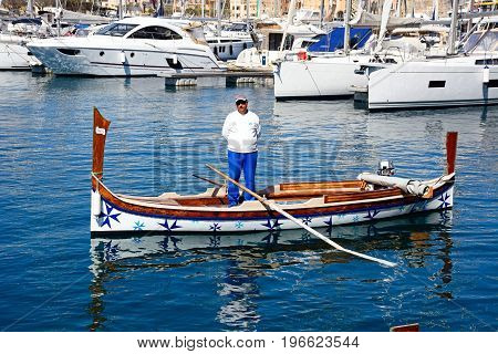 VITTORIOSA, MALTA - MARCH 31, 2017 - Oarsman standing in a traditional Maltese Dghajsa water taxi in the harbour with views towards Senglea waterfront Vittoriosa Malta Europe, March 31, 2017.