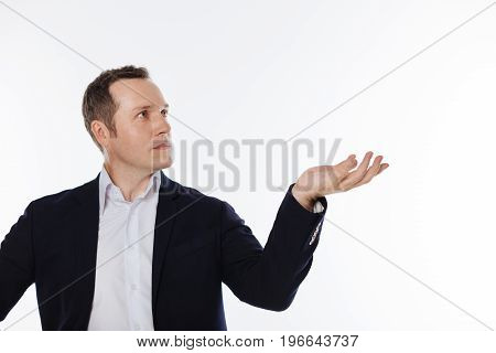 Big object. Concentrated diligent classy man pretending demonstrating something while looking at it and standing isolated on white background