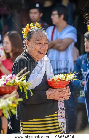 CHIANGMAI THAILAND - JANUARY 25 2015: Smiling indigenous senior woman with tray with pedestal of flowers in parade of 22nd Traditional Skirt Fabric and The Indigenous Product and Culture Festival in Mae Chaem Chiangmai Thailand