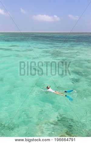 Woman snorkeling in clear shallow sea of tropical lagoon with turquoise blue water and coral reef, near exotic island. Mnemba island, Zanzibar, Tanzania.