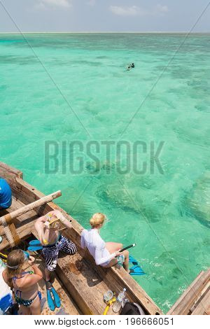 Woman snorkeling in clear shallow sea of tropical lagoon with turquoise blue water and coral reef, near exotic island. Mnemba island, Zanzibar, Tanzania.