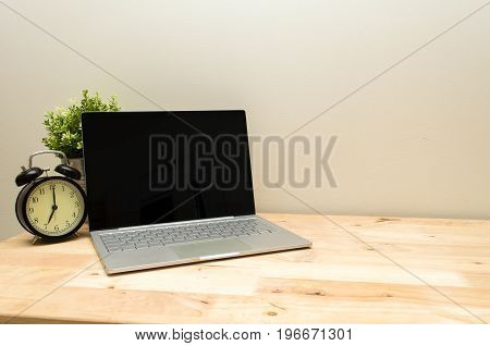 Laptop notebook computer and black vintage retro alarm clock times at 7 o'clock morning on wooden table workspace selective focus copy space vintage color tone