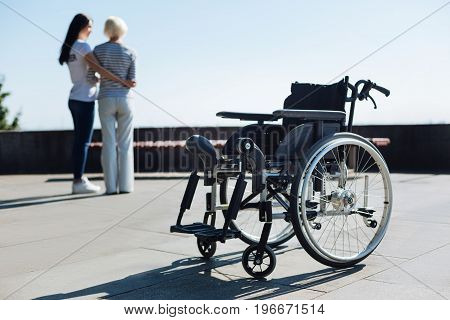 I got your back. Dynamic radiant aged woman wanting enjoying the view from a viewpoint and standing up from a wheelchair while young woman supporting her