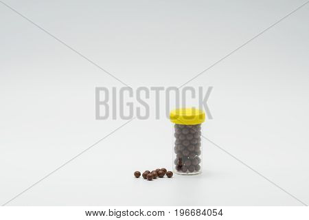 Thai herbal medicine in plastic bottle with modern design and many pills spread on a white background bolus
