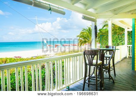 Turks and Caicos Island, July 10, 2012; Shady tropical veranda seats overlooking sun umbrellas on Caribbean beach and ocean blue sky and horizon.