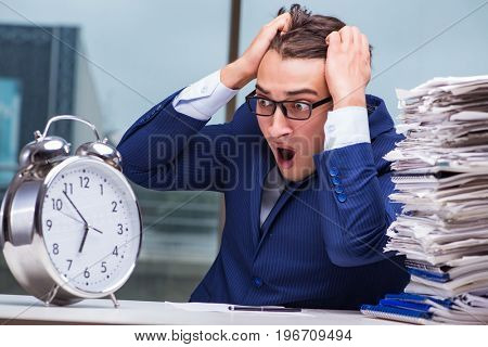 Businessman with pile stack of paper paperwork and an alarm cloc