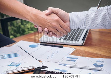Close-up of two business people shaking hands while sitting at the working place. Two confident executives business colleagues meeting and discussing ideas of project about company offer.