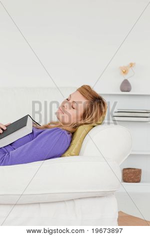Donna attraente sdraiato sul divano che è caduto addormentata durante la lettura di un libro