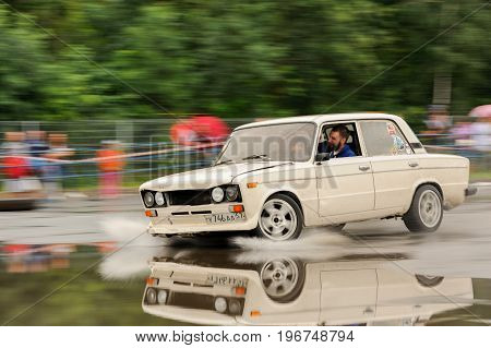 Orel Russia July 22 2017: Dynamica car festival. White tuned Russian car VAZ Lada rides on puddles and reflects in wet asphalt motion blur